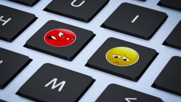 Two computer keys with an angry emoji looking at a sad emoji